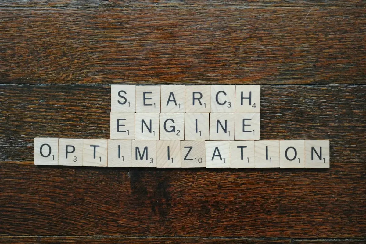Letras de Scrabble em madeira dispostas sobre uma mesa e que formam "SEARCH ENGINE OPTIMIZATION" (SEO). (Imagem: Sarah B/Unsplash)